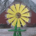 This is a picture of a windmill covered in ice from freezing rain with a red barn in the background.